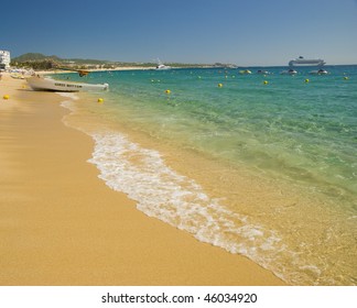 Beach With Crystal Clear Water. Cabo San Lucas, Mexico. A Cruise Ship And A Fishing Boat Can Be Seen In The Background