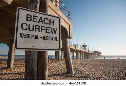 Beach Curfew Times On Sign Under The Pier Of Huntington Beach In Southern California