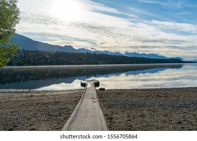 Beach and dock with reflection of mountains in Windermere Lake in Invermere, British Columbia, Canada.