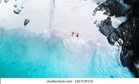 Beach drone view tropical island, white beach with waves, couple lay down on the beach man and woman