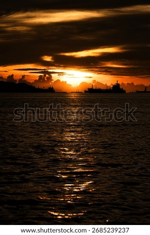 At the beach in the evening when the sun is setting. There is a cool breeze and boats sail past.
