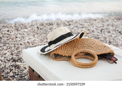 Beach flat lay accessories: straw hat, summer knitted bag, and sunglasses on sunbed near the sea on the pebble beach.  - Powered by Shutterstock