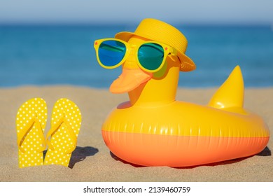 Beach flip-flops and yellow duck on the sand against blue sea and sky background. Summer vacation concept