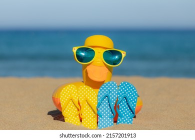 Beach flip-flops and yellow duck on the sand against blue sea and sky background. Summer vacation concept
