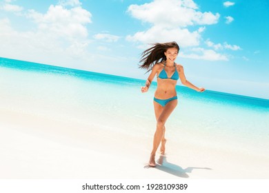 Beach fun happy Asian woman laughing running in blue bikini from ocean Caribbean travel destination. Slim body model enjoying summer holidays.