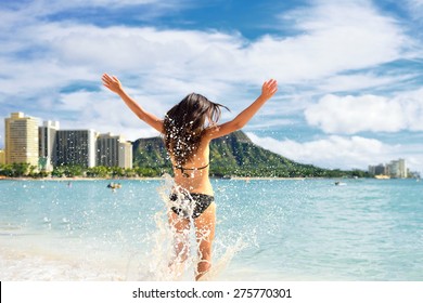 Beach Fun - Happy Woman On Hawaii Waikiki Vacation. Unrecognizable Young Adult From Behind Jumping Of Joy In Water Waves, Arms Up With Diamond Head Mountain In The Background, Landmark Of Honolulu.