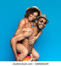 Beach Fun. Millennial Black Couple Fooling, Guy Giving His Girlfriend Piggyback Ride, Blue Studio Background