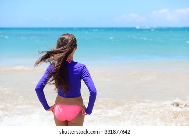 Beach Girl Going Swimming In Rashguard Swimwear Protective Clothing. Woman Standing In Bikini And Uv Sun Protection Surf Shirt Looking At Ocean Waves. Healthy Active Lifestyle.