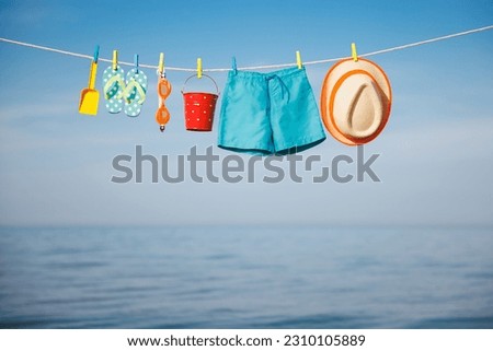 Beach hat, flip-flops and goggles hanging on a clothesline. Things for vacation against blue sky and sea. Summer holiday and travel concept