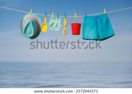 Beach hat, flip-flops and goggles hanging on a clothesline. Things for vacation against blue sky and sea. Summer holiday and travel concept