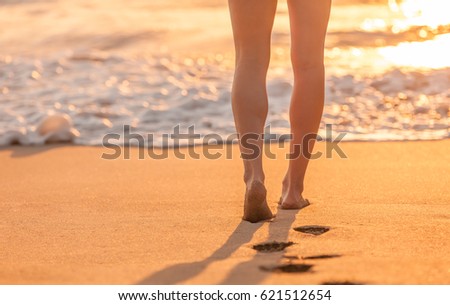 Beach holidays. Closeup of woman's feet walking down a tropical sandy beach at sunset. 