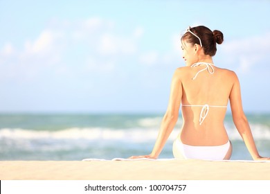 Beach holidays woman enjoying summer sun sitting in sand looking happy at copy space. Beautiful young bikini model. Mixed race Caucasian / Asian Chinese.