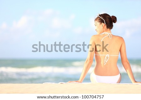 Beach holidays woman enjoying summer sun sitting in sand looking happy at copy space. Beautiful young bikini model. Mixed race Caucasian / Asian Chinese.