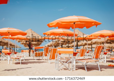 Beach in Italy. Orange umbrellas and deck chairs on the sand against the sea. Summer time