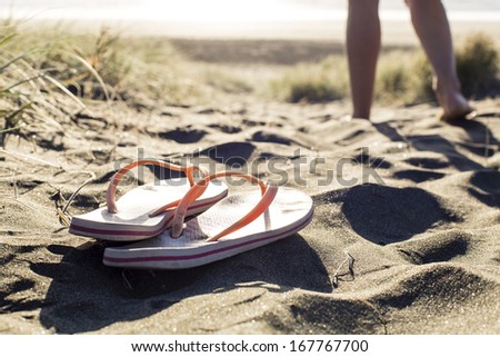 Beach Jandals/ a woman leaves her Flip-flops on the dry sand to go for a swim