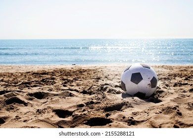 beach landscape with a soccer ball on the sand under a summer sun and in the background the water and the blue sky