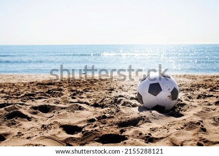 beach landscape with a soccer ball on the sand under a summer sun and in the background the water and the blue sky