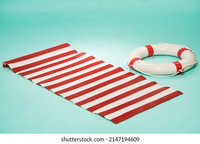 beach mat in red and white stripes and a life buoy on a turquoise pin-up background - Shutterstock ID 2147194609