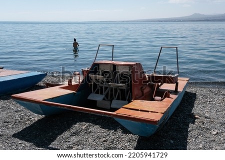 Beach on Sevan lake with old paddle boat (pedalo, water bike) on pebble and girl in the water on sunny summer day, Armenia.