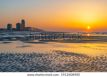The beach of Ostend city at sunset with unsharp foreground by the North Sea with the urban skyline of sea view apartments, West Flanders, Belgium.