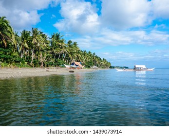Beach with palm trees and a traditional wooden Philippine boat in Donsol, Philippines