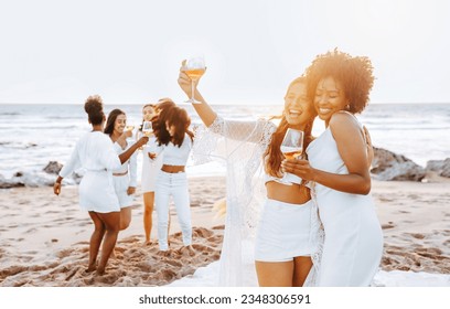 Beach party. Group of young diverse ladies dancing and drinking champagne on the beach at sunset, celebrating bachelorette party and having fun by ocean shore - Powered by Shutterstock