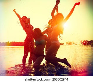 Beach Party. Teenage girls having fun in water. Group of happy young people dancing at the beach on beautiful summer sunset. Silhouettes of group of teen girls jumping and dancing. Joyful friends - Powered by Shutterstock