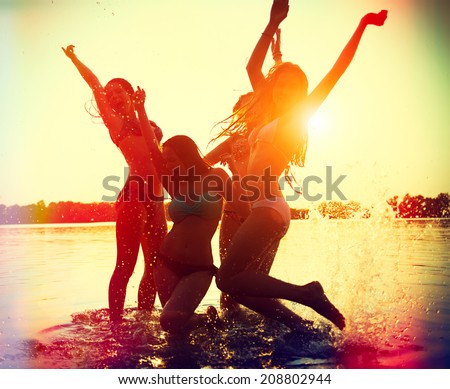 Beach Party. Teenage girls having fun in water. Group of happy young people dancing at the beach on beautiful summer sunset. Silhouettes of group of teen girls jumping and dancing. Joyful friends