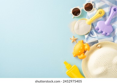 Beach play essentials for kids. Top view of sand toys: shovel, rake, crab mold, SPF cream, straw hat, sunglasses, beach blanket, shell, starfish on pastel blue with copy space - Powered by Shutterstock