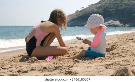 Beach playtime delight for little sisters, little girl with baby playing with sand on the beach - Powered by Shutterstock