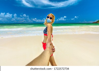 Beach relax in Covid-19 time: tourist woman sunbathing holding hand of her partner at Seychelles beach with a surgical mask. Coronavirus quarantine. Holidays and travels in the COVID pandemic. - Powered by Shutterstock