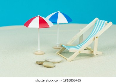 Beach relaxation and vacation concept. Toy sun lounger and umbrella on sand and colorful paper background.