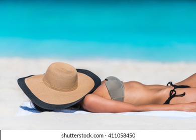 Beach relaxation woman sleeping sun tanning covering her face with straw hat for uv solar protection on caribbean destination blue ocean background. Vacation girl relaxing resting on summer travel. 