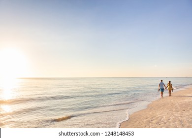 Beach relaxing vacation - travel tourists couple walking on beach at sunset landscape background. Summer holidays destination.