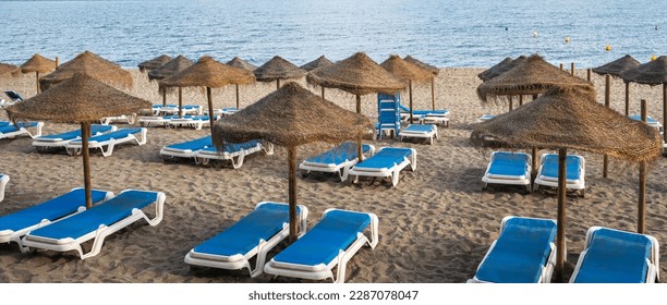 Complejo de playa, concepto de vacaciones de verano en el mar. Tumbonas de madera con sombrillas. Una hilera de tumbonas en un complejo de playa.