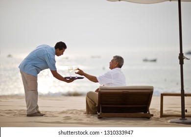 Beach Resort Waiter Serving Wine To Man On Sun Lounger