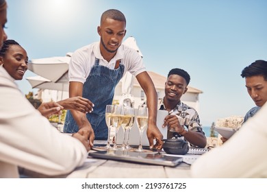 Beach Restaurant, Waiter And Champagne Celebration With Friends. Hospitality, Fine Dining And A Relaxing Outdoor Meal With People. Summer Holiday Or Lunch Break Outside With View Of The Ocean.