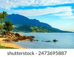 Beach with rocks and palm trees on the island of Ilhabela on the north coast of Sao Paulo with the mountains in the background