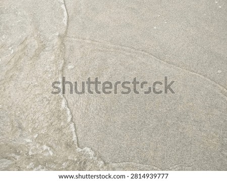Beach sand with a thin layer of water forms fine ripples and smooth natural patterns.