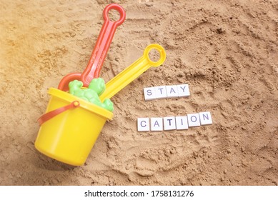 Beach Sand With Toys For The Baby, Water, The Word Holi Stay In Colored Letters. Staycation Content