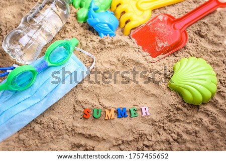 Beach sand with toys for the baby, water, the word summer in colored letters. Staycation content