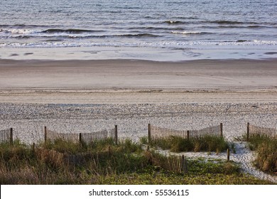 Beach scene of sand,surf,dune,sea grass,fence as early morning welcomes a beautiful day at the beach.