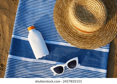 Beach scene with sunblock bottle, striped towel, stylish sunglasses, straw hat on sandy background. Accessories for skin protection against summer sun, holiday vacation concept by sea. - Powered by Shutterstock