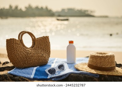 Beach scene with sunscreen bottle, straw hat on blue towel. Protective sunblock essential for tropical climate. UV protection gear, sunglass on sunny ocean shore. Holiday, skin care, leisure concept. - Powered by Shutterstock