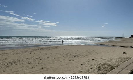 A beach scene with waves crashing against rocks, people standing near bicycles, and a cloudy sky. It is interesting for its depiction of a tranquil coastal environment. - Powered by Shutterstock