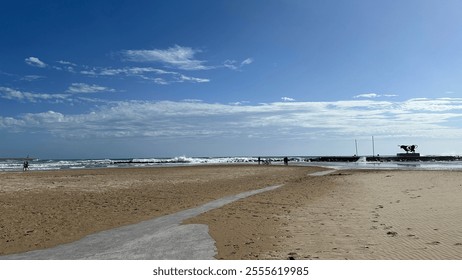 A beach scene with waves crashing against rocks, people standing near bicycles, and a cloudy sky. It is interesting for its depiction of a tranquil coastal environment. - Powered by Shutterstock