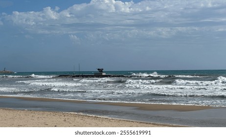 A beach scene with waves crashing against rocks, people standing near bicycles, and a cloudy sky. It is interesting for its depiction of a tranquil coastal environment. - Powered by Shutterstock