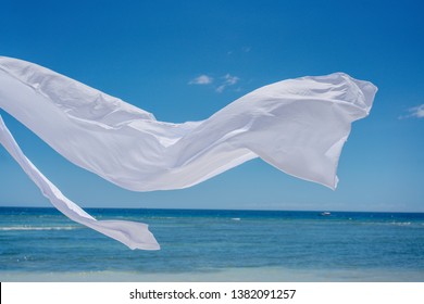 Beach shade with white gracefully fluttering fabric curtains on seashore. Sea breeze and white sand. Close up.
