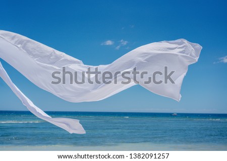 Beach shade with white gracefully fluttering fabric curtains on seashore. Sea breeze and white sand. Close up.
