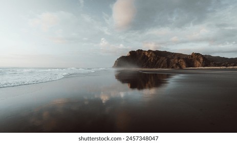 Beach side cliffs reflected on the black sand beach during the sunset
